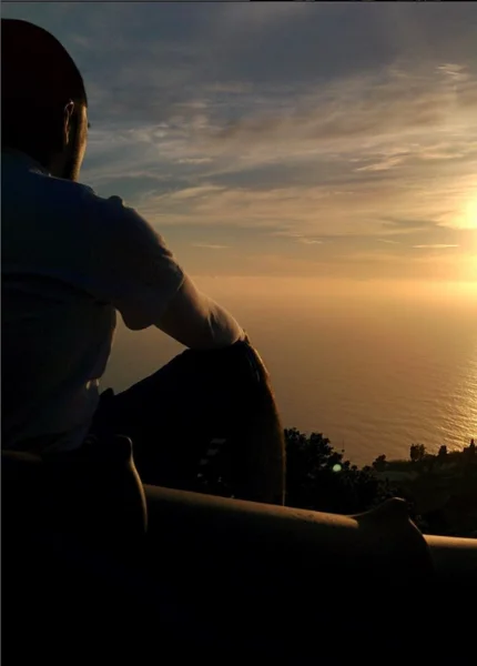 a man sitting on a ledge looking at the sunset